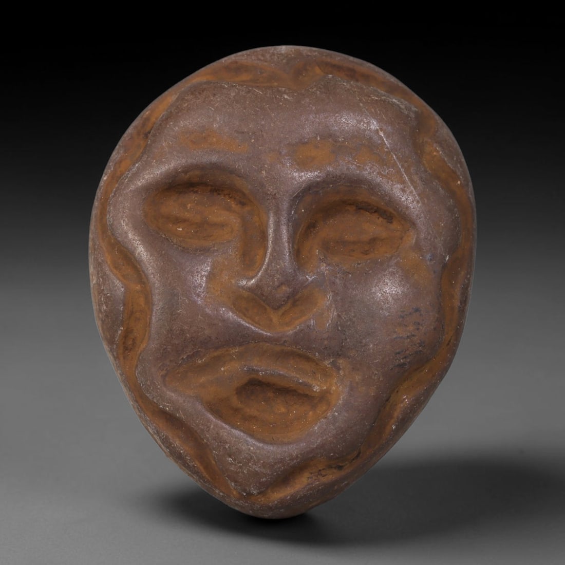 Ancient Medieval Mediterranean Hand Carved Stone Maskette Amulet, 51AP: Miniature wearable sacred talisman hand hewn from natural soft stone, originating from Medieval Mediterranean cultural craft traditions. Small carved stone amulets were widespread personal artifacts a