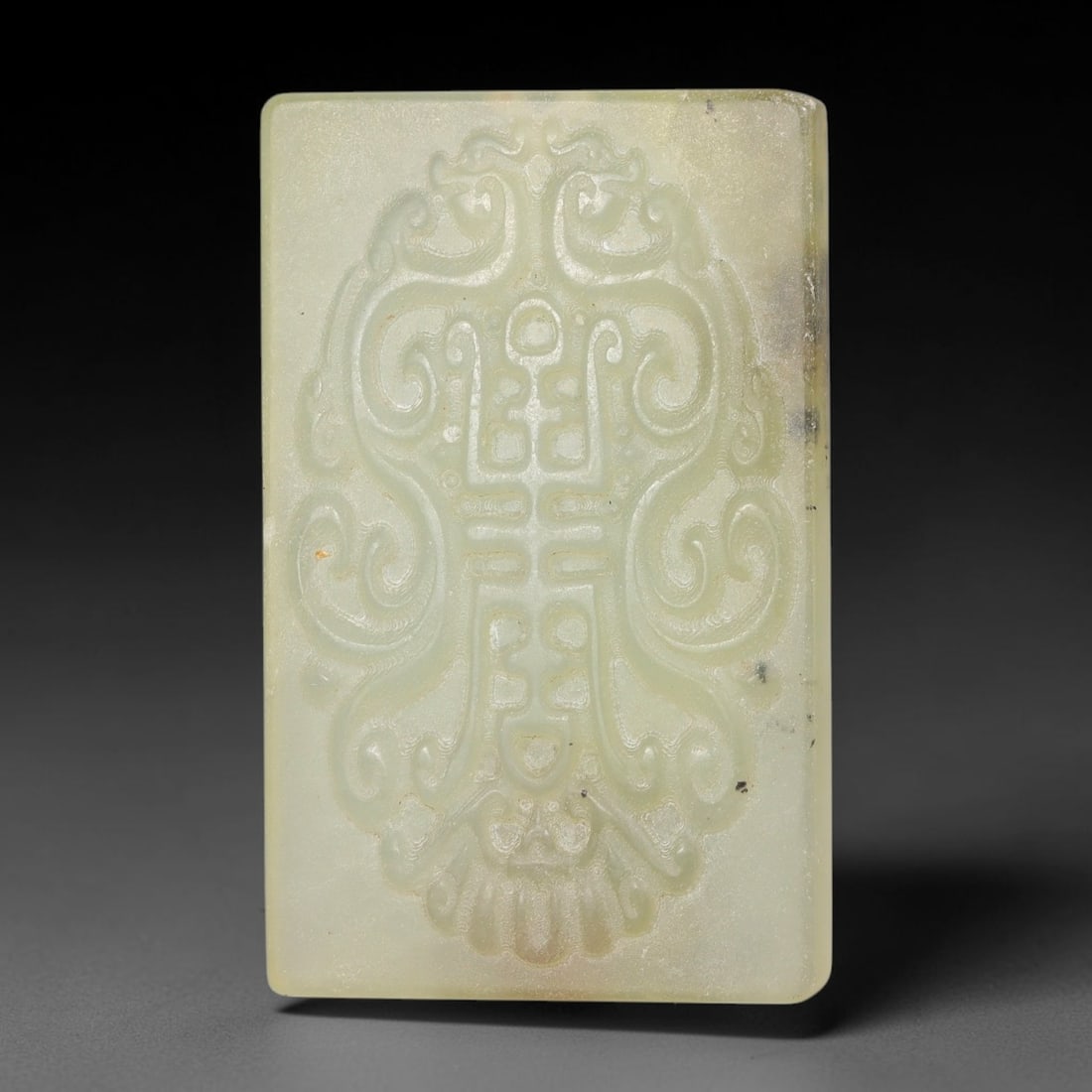 Chinese Nephrite Jade Plaque - Shou Character Scroll Tablet, 7AE: Formed from natural pale celadon nephrite jade with faint dark mineral flecks dispersed across the stone surface, this rectangular tablet features refined low-relief carving with consistent delicate i