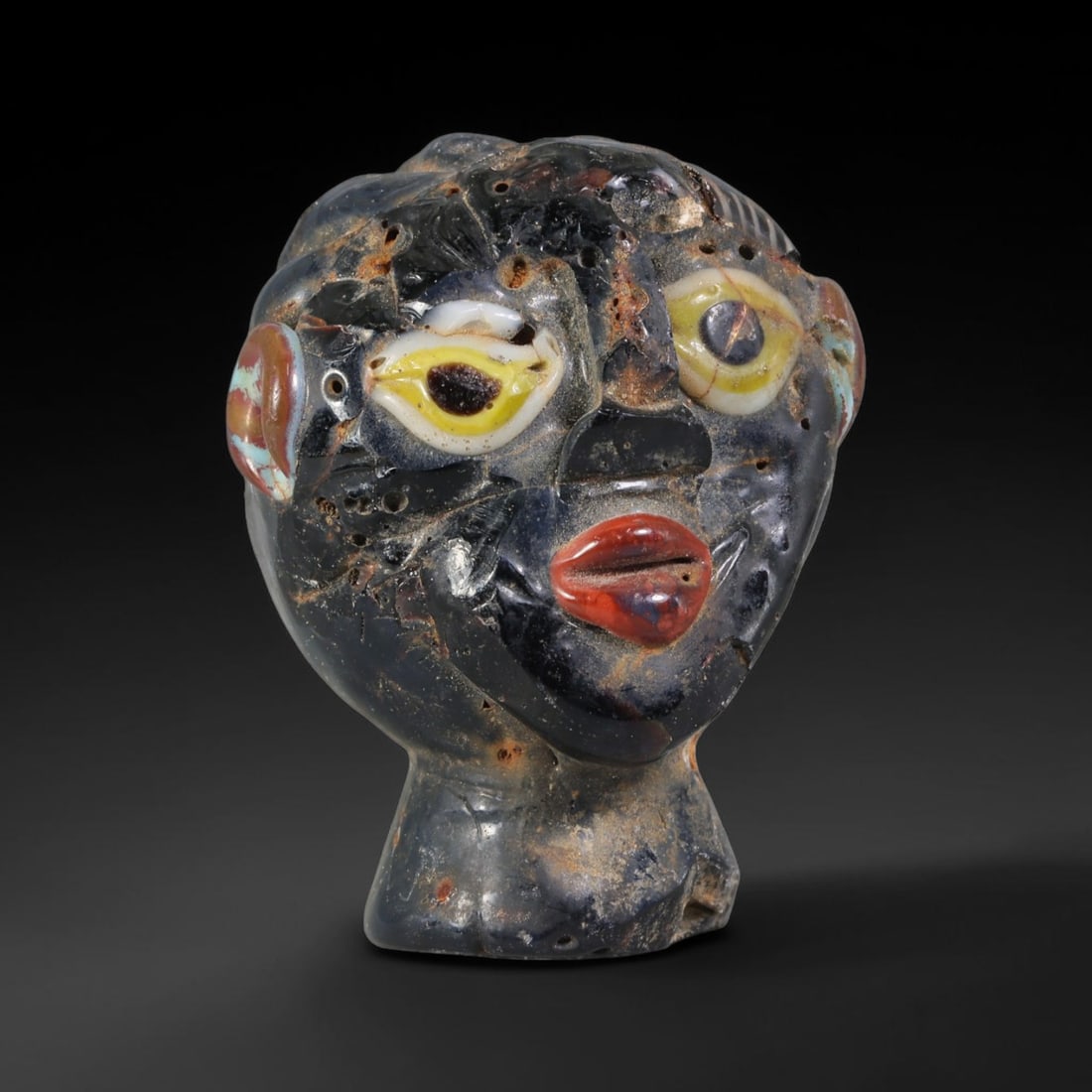 Ancient Canaanite & Phoenician Cultures Polychrome Glass Human Head Bead (3000-300 BCE), 35AE: This antique polychrome glass human head bead originates from Canaanite & Phoenician Cultures, the ancient Levantine maritime civilization celebrated as pioneering glass bead craft and Mediterranean l
