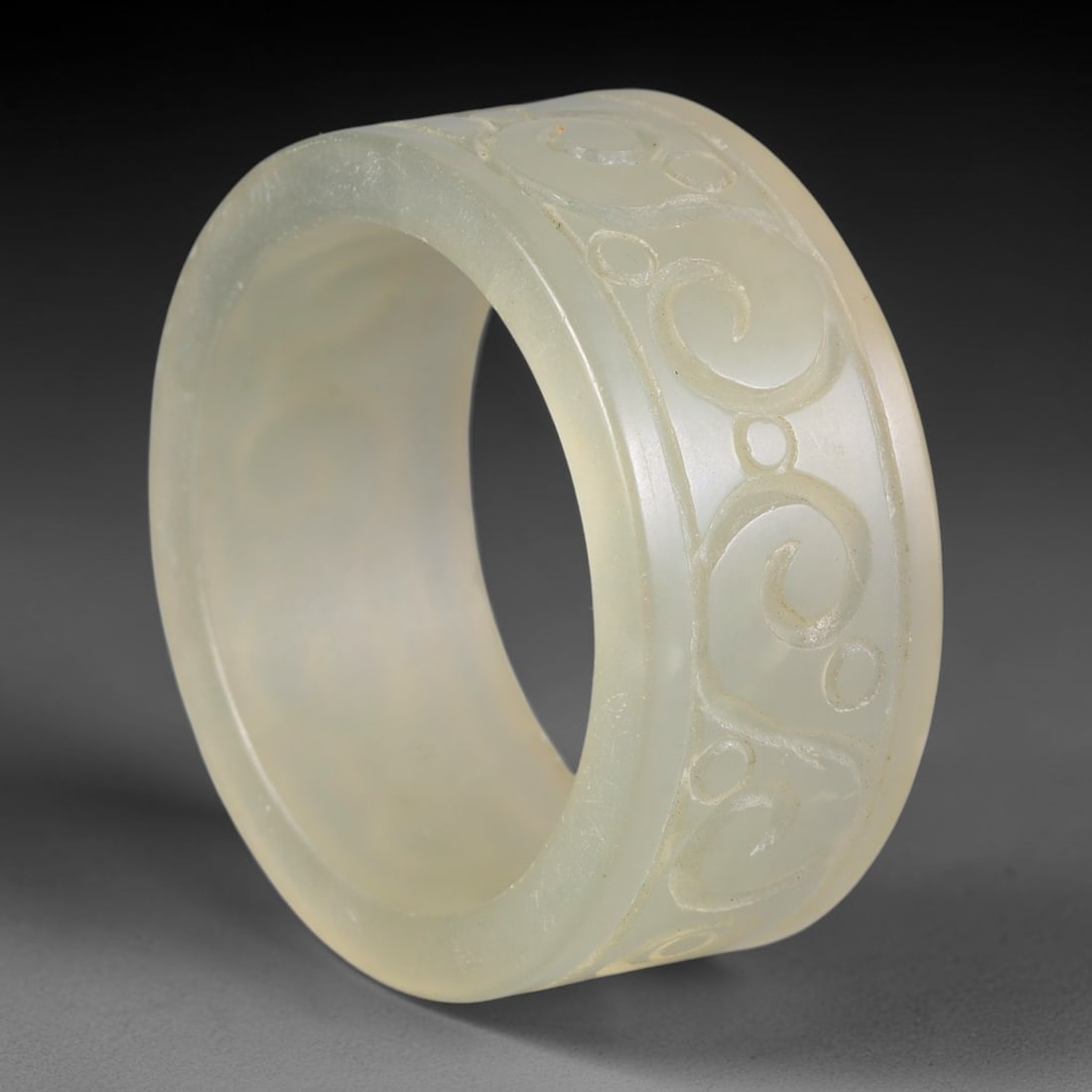 Chinese Nephrite Jade Cylinder - Scroll Incised Decorative Form, 12AE: Crafted from translucent pale celadon nephrite jade with faint natural mineral flecks throughout the stone matrix, this hollow cylindrical stone form displays continuous hand-incised spiral scroll and