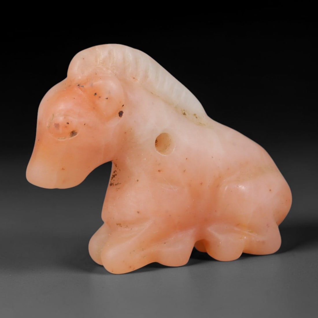 Ancient Western Asiatic Recumbent Beast Zoomorphic Amulet (1000-600 BCE), 17AB: Hand-carved translucent pale pink hardstone pendant sculpted as a resting horse figure with fine linear incisions detailing its mane and subtle indentations marking facial features. A cleanly drilled 