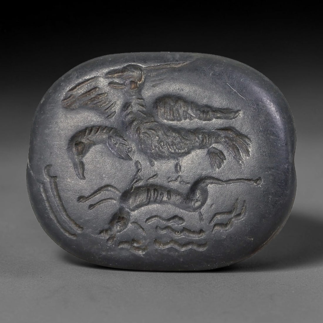 Ancient Sasanian Dark Steatite Mythical Creature Intaglio Seal Pendant (224-651 CE), 82AE: Smooth oval dark steatite stone intaglio talisman with side perforation for suspension. Deep recessed engraving depicts layered mythical zoomorphic figures including winged avian beasts and aquatic se