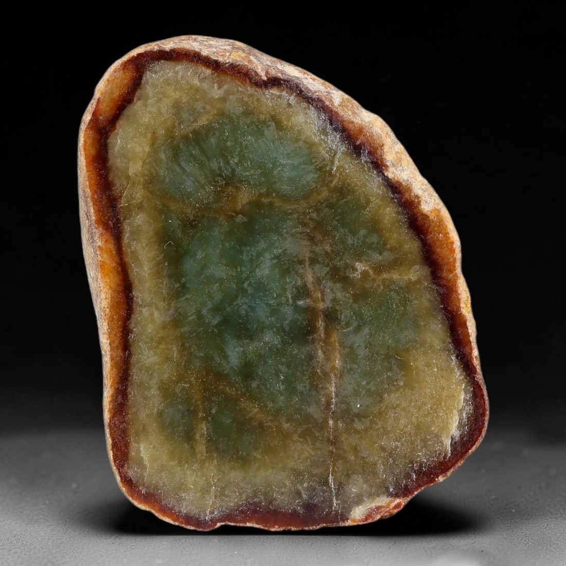 225ct Natural Type A Burmese Dark Red Skin Rim Olive Green Jadeite Jade Sliced Rough, 3FA: This specimen is a natural sliced rough pebble of untreated Type A Burmese jadeite, wrapped by a distinct deep reddish-brown oxidized skin rim around its polished cut face. The interior displays semi-