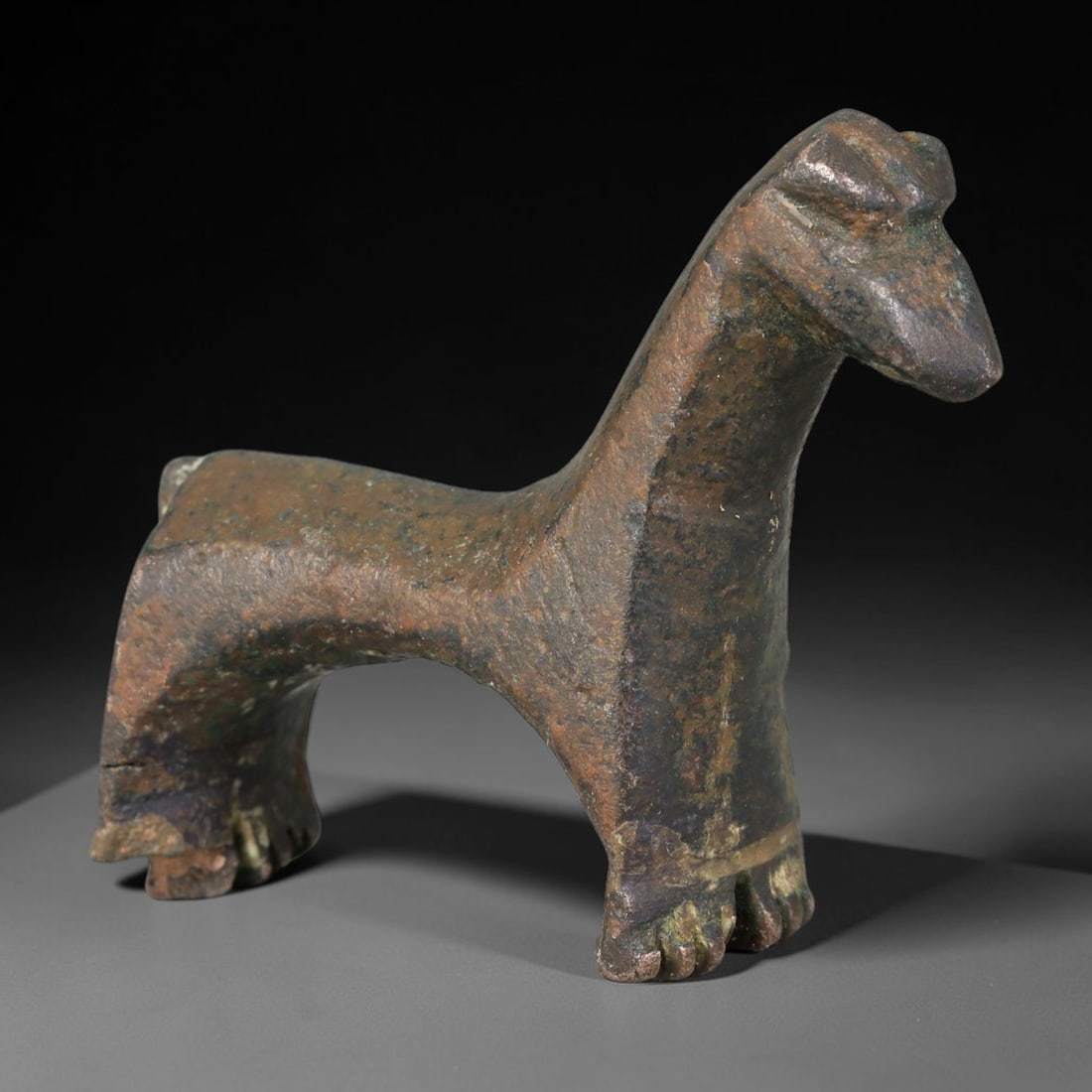 Ancient Near Eastern Cast Bronze Stylized Horse Figurine (900-500 BCE), 40AB: Miniature solid cast bronze statuette of a stylized standing horse with an elongated arched neck, geometric simplified torso and blocky legs detailed with incised hoof lines. The surface bears heavy a