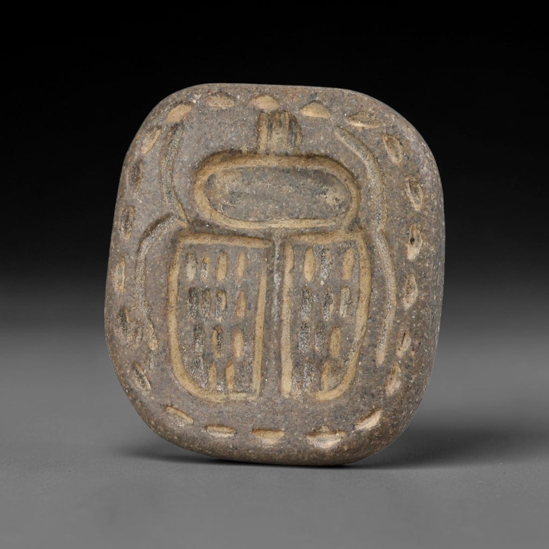 Ancient Egyptian Grey Stone Scarab Motif Stamp Seal (664-30 BCE), 80AB: This granular grey stone stamp seal features a deeply incised scarab beetle design encircled by dotted border detailing on its impression face. The reverse bears a central pierced suspension knob for 