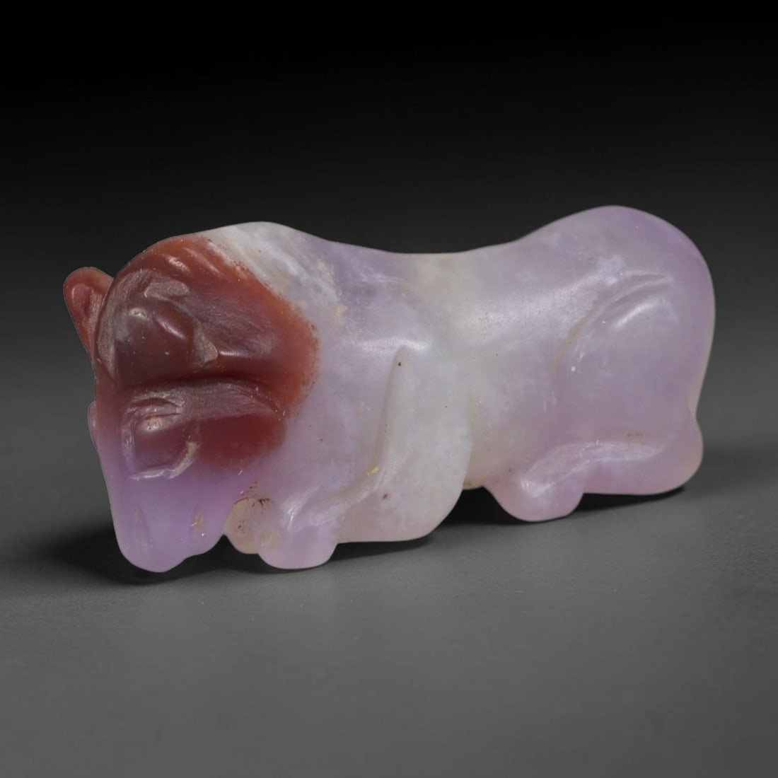 Ancient Sasanian Persian Natural Purple Banded Agate Recumbent Bull Amulet (224-651 CE), 34AB: Hand-carved from natural purple banded agate with distinct reddish-brown colouration concentrated at the bovine's head, this small recumbent bull figurine served as a protective talisman in Sasanian P
