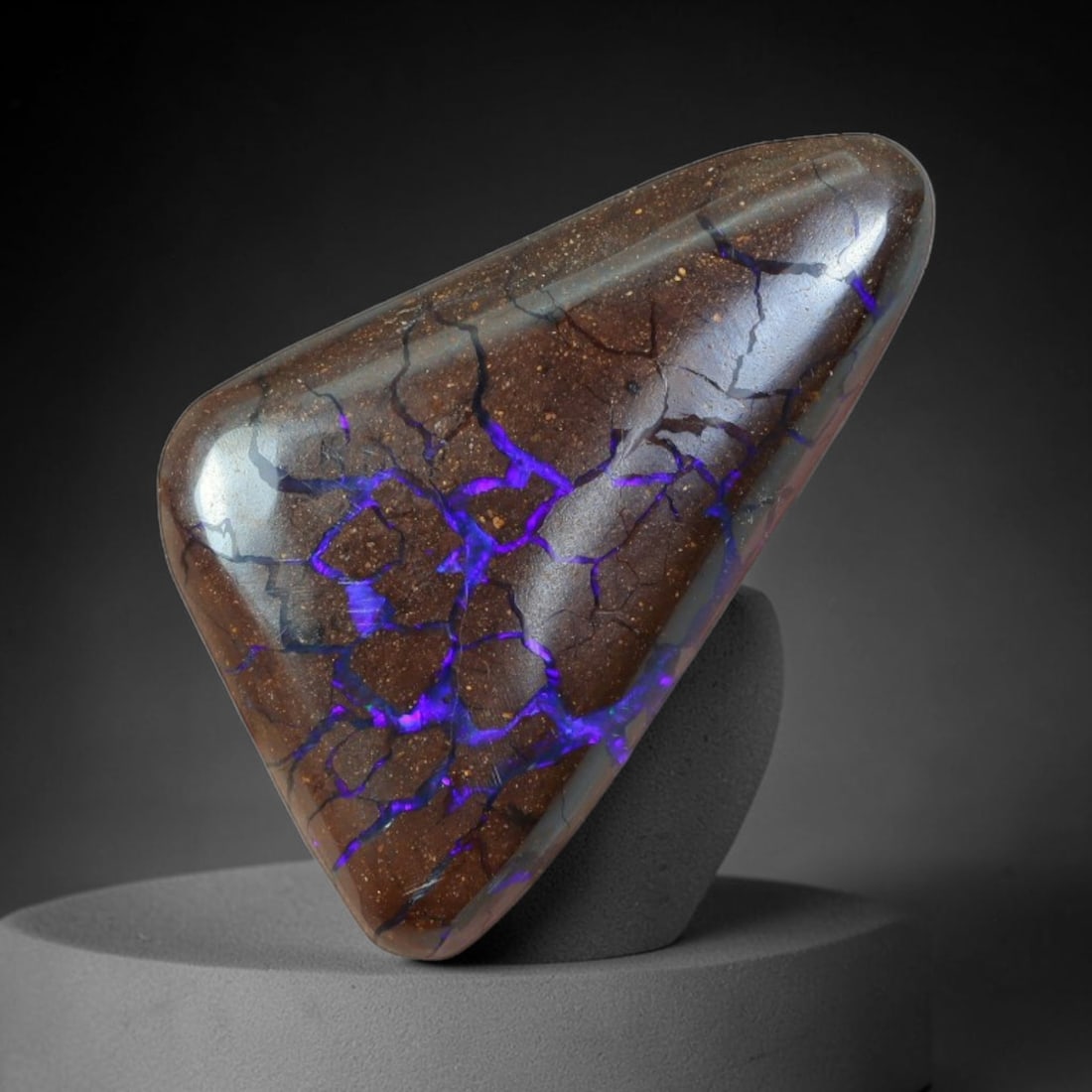 17.40ct Natural Australian Queensland Matrix Boulder Opal Cabochon, 65AT: Hand polished freeform triangular cabochon of natural Queensland matrix boulder opal, set upon fine speckled ironstone host rock crisscrossed with vivid saturated violet-purple opal vein networks form