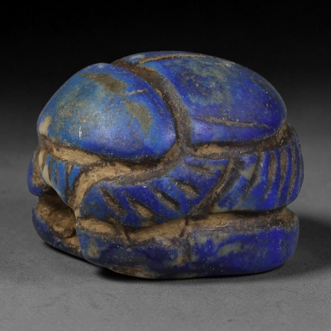 Ancient Egyptian Late Period Natural Lapis Lazuli Scarab Amulet (664-30 BCE), 53AB: Miniature hand-carved scarab talisman crafted from vivid royal blue lapis lazuli, complete with finely incised linear detailing to define the beetle's head, legs and wing casings. Earthy burial sedime