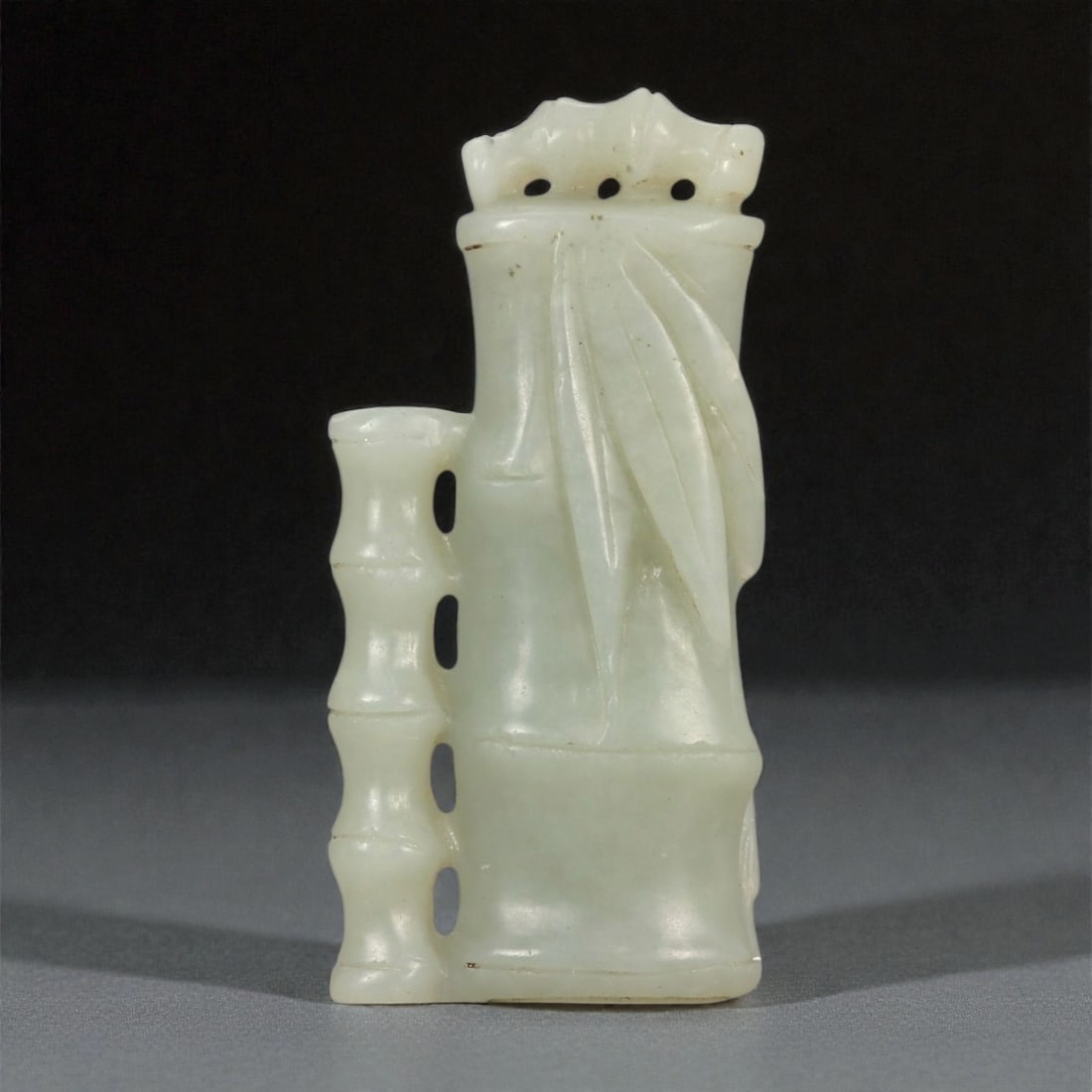 A Chinese Hetian Nephrite Jade Bamboo-Form Pendant, 73FA: Carved from pale celadon nephrite jade with soft translucency and a smooth, satin polish, the pendant is modeled in the form of a segmented bamboo stalk with an attached shoot. The main shaft is rende