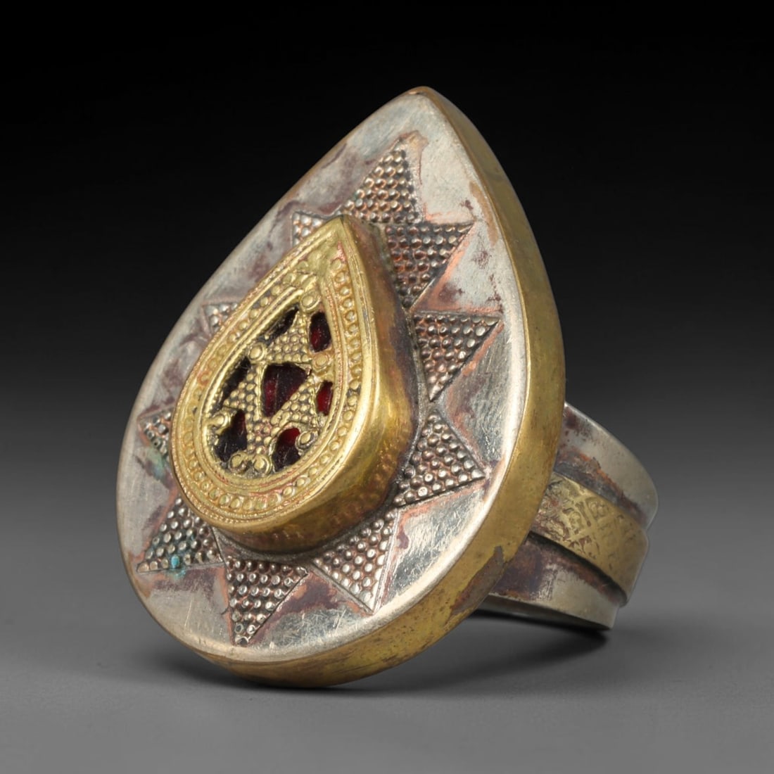 Antique Central Asian Mixed Metal Teardrop Star Inlaid Statement Ring, 88AA: Handcrafted antique Central Asian tribal signet ring with a 3.8cm x 2.8cm teardrop shaped ring face, forged from silvered base metal paired with thick gilded overlay accents and inset deep red decorat