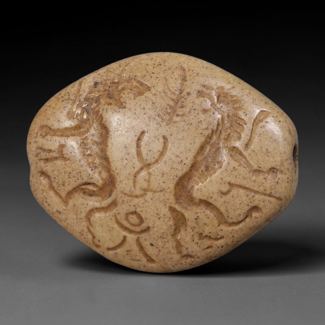 Ancient Sasanian Speckled Stone Dual Winged Beast Intaglio Pendant Seal (224-651 CE), 81AE: Oval polished speckled beige stone intaglio talisman seal, horizontally drilled for suspension. Recessed engraving features two confronting winged mythical beasts flanking abstract symbolic emblems, c