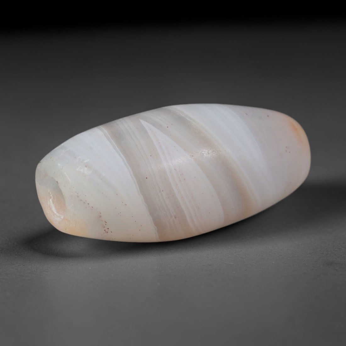 Ancient Mughal Cambay Gujarat Banded Agate Barrel Bead (1526-1800 CE), 50AD: This antique banded agate barrel bead originates from the renowned Cambay lapidary workshops of Mughal-era Gujarat, a historic production center for fine chalcedony adornments circulated across Indian