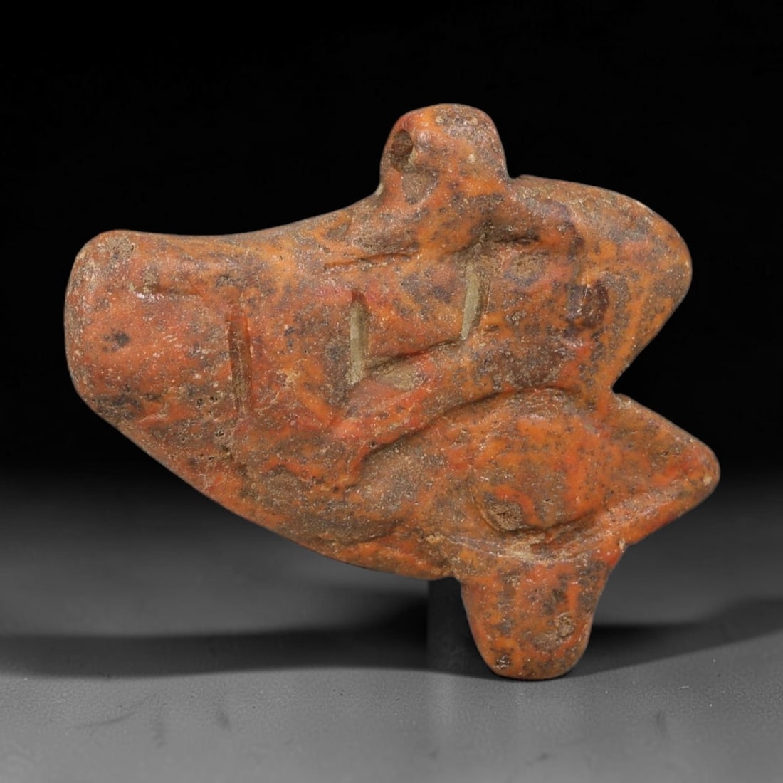 Ancient Egyptian Late Period Red Speckled Stone Wedjat Eye Amulet (664-30 BCE), 86AE: Hand-carved mottled reddish hardstone Wedjat Eye of Horus protective amulet, featuring deeply recessed carving forming the traditional eye, brow and teardrop motif. An integrated pierced suspension lu