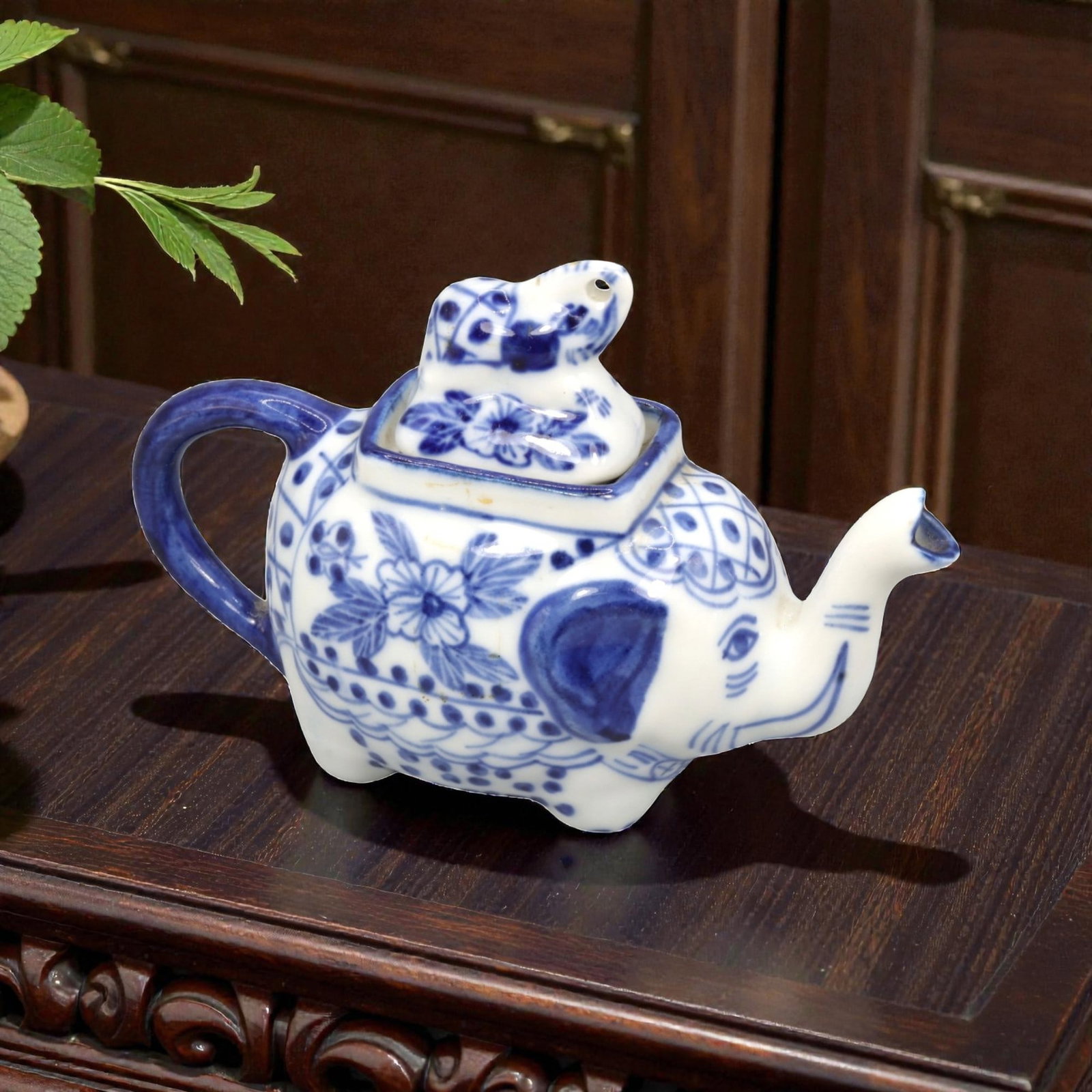A Chinese Porcelain Elephant-Form Teapot, 20th Century, 46FK: Modeled in the form of a recumbent elephant, the teapot is constructed from white porcelain and decorated in underglaze cobalt blue. The elephant's raised trunk functions as the spout, while a looped 