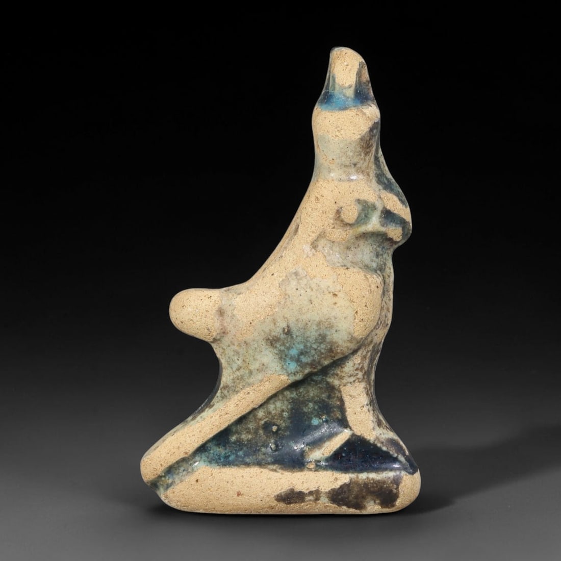 Ancient Egyptian Faience Horus Falcon Amulet (664-30 BCE), 74AB: Molded pale clay faience amulet shaped as the sacred Horus falcon, finished with mottled turquoise and dark indigo glaze showing heavy age wear and glaze loss revealing the porous clay core. The compa