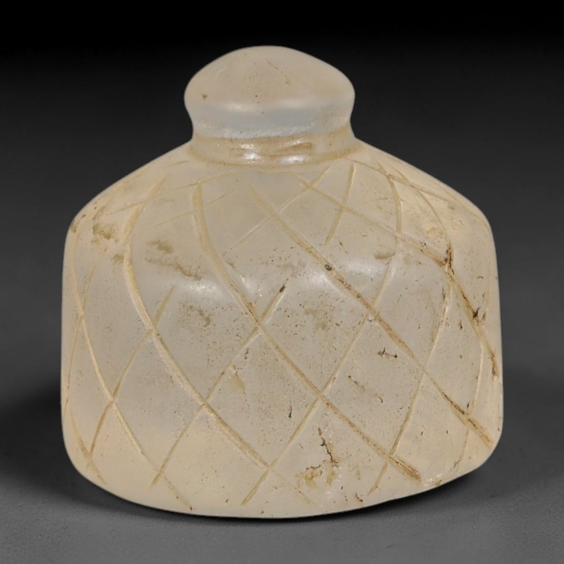 Ancient Medieval Mamluk Islamic Frosted Glass Bell Form Talisman (1250-1517 CE), 98AE: Miniature bell-shaped talisman hand-carved from translucent pale frosted glass, fully decorated with intersecting incised lattice diamond patterns covering the domed body. A smooth rounded suspension 
