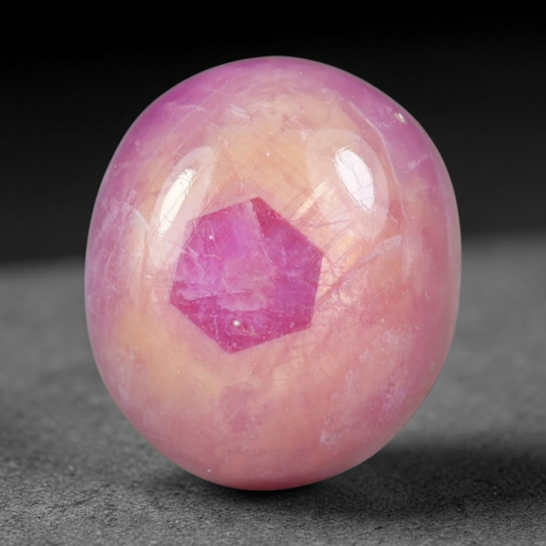 15.03 Carats Natural Madagascar Soft Rose Pink Heated Ruby Cabochon Loose Gemstone, 100AH: This warm blush-toned ruby cabochon carries blended swathes of soft rose pink and gentle peach undertones, with faint natural mineral veining throughout the polished dome, measured at 14.3x12.4x7.3mm.