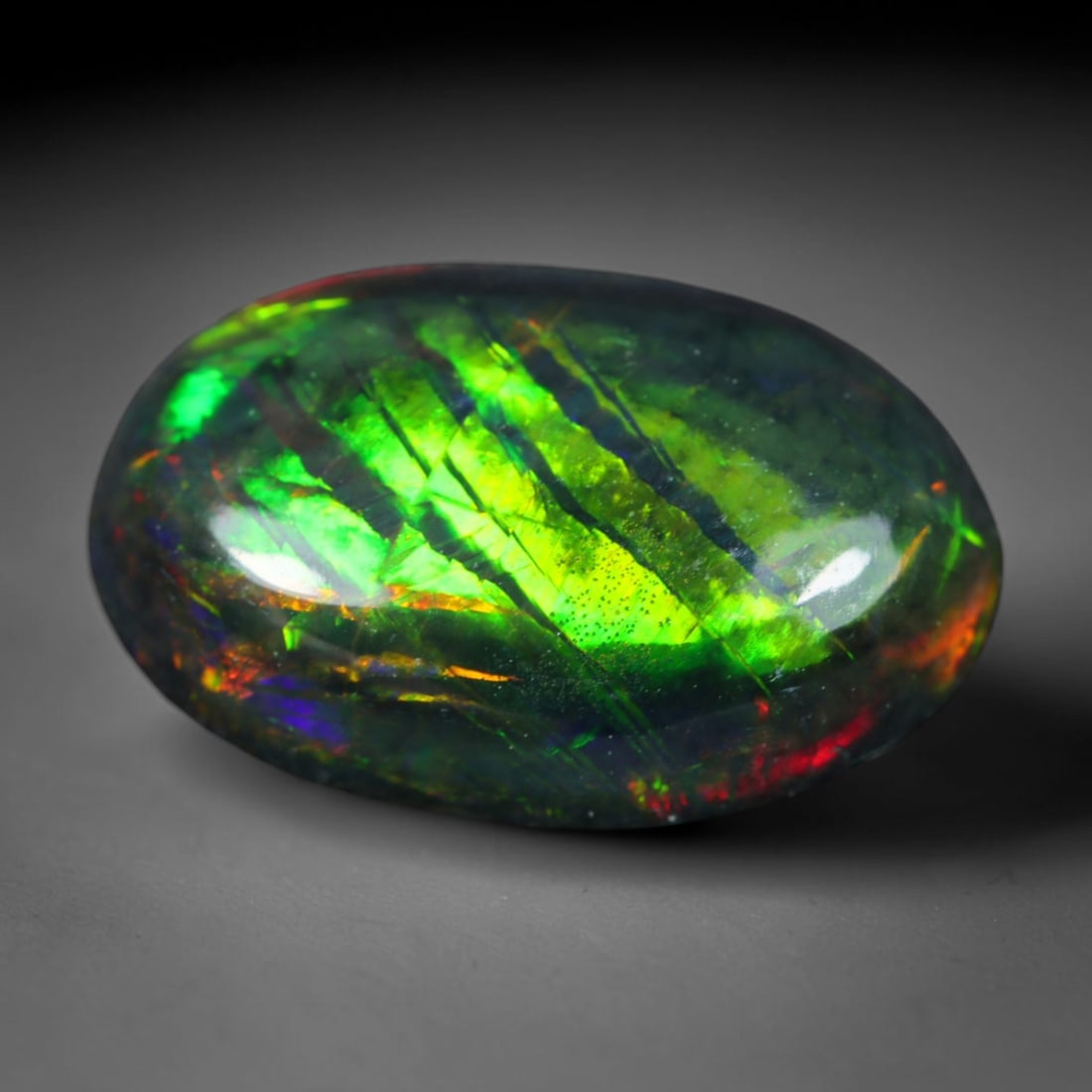 2.02ct Natural Ethiopian Welo Black Smoked Opal Cabochon Loose Gemstone, 87AK: This fully polished Ethiopian Welo opal features a dark smoked base with vivid, sweeping play-of-color shifting across its glossy dome surface, measured at 13.2x8.6x4mm. The black smoke treatment deep