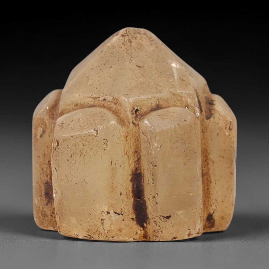 Ancient Medieval Mamluk Islamic Rock Crystal Pyramidal Talisman (1250-1517 CE), 64AL: Hand-carved miniature protective amulet from translucent pale rock crystal, shaped into a geometric multi-lobed pyramidal form with segmented vertical faceting rising to a sharp apex. Deep amber-brown