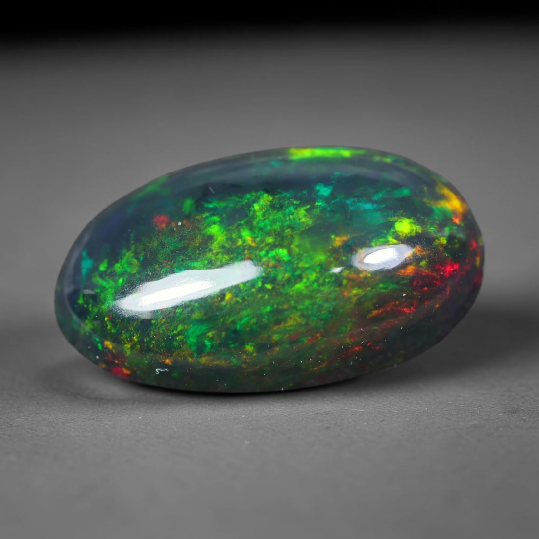 3.08ct Natural Ethiopian Welo Black Smoked Opal Cabochon Loose Gemstone, 27FL: This fully polished Ethiopian Welo opal features a dark smoked base with vivid, sweeping play-of-color shifting across its glossy dome surface, measured at 14.1x8.3x5mm. The black smoke treatment deep
