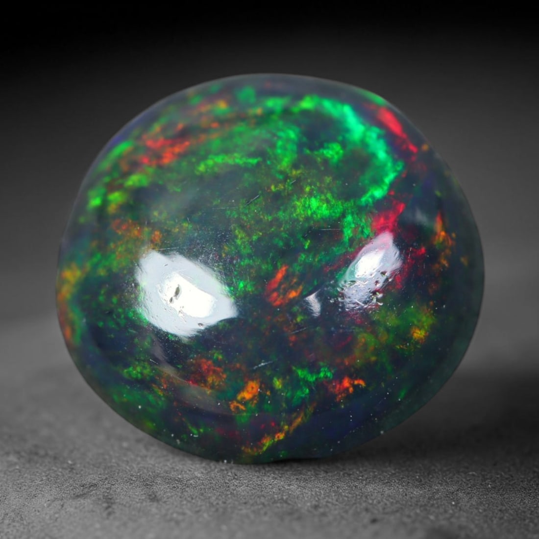1.56ct Natural Ethiopian Welo Black Smoked Opal Cabochon Loose Gemstone, 5FL: This fully polished Ethiopian Welo opal features a dark smoked base with vivid, sweeping play-of-color shifting across its glossy dome surface, measured at 9.2x9x3.7mm. The black smoke treatment deepe