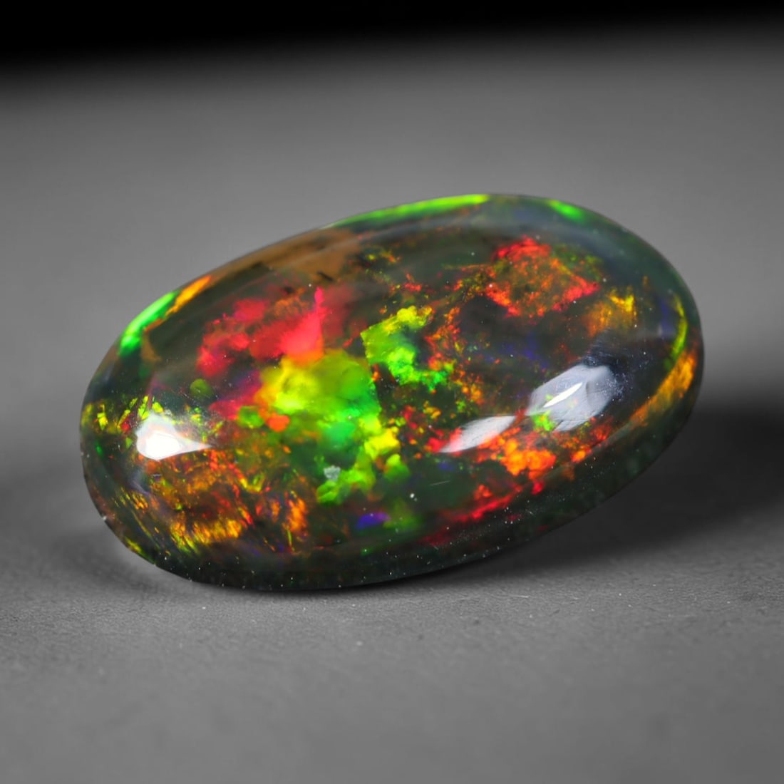1.83ct Natural Ethiopian Welo Black Smoked Opal Cabochon Loose Gemstone, 6FL: This fully polished Ethiopian Welo opal features a dark smoked base with vivid, sweeping play-of-color shifting across its glossy dome surface, measured at 12.4x7.5x3.5mm. The black smoke treatment de