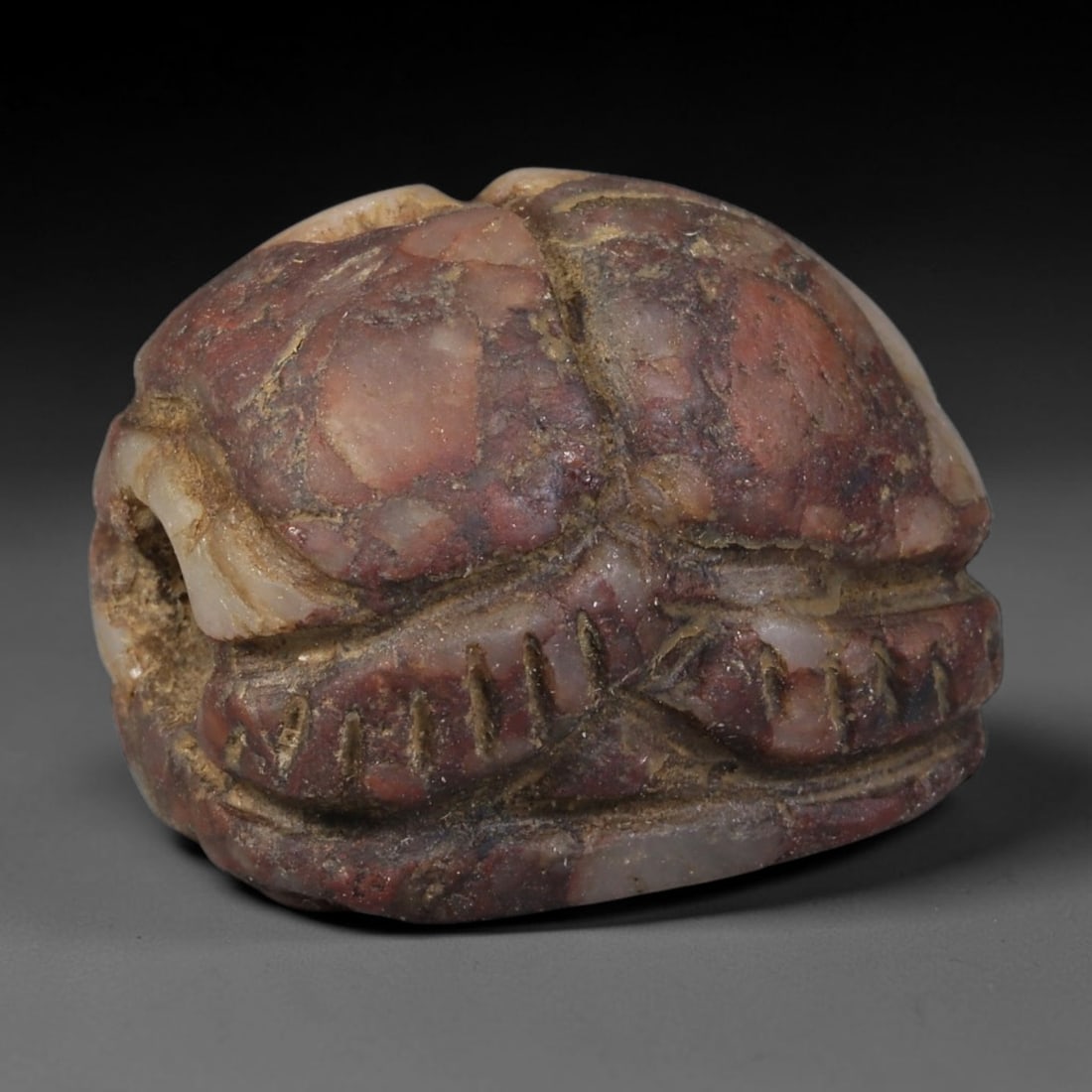 Ancient Egyptian Late Period Natural Red Banded Stone Scarab Amulet (664-30 BCE), 55AB: Miniature hand-carved scarab talisman crafted from mottled red-and-pink banded hardstone, fully horizontally pierced for threading as a wearable funerary pendant. Crisp incised linear detailing marks 