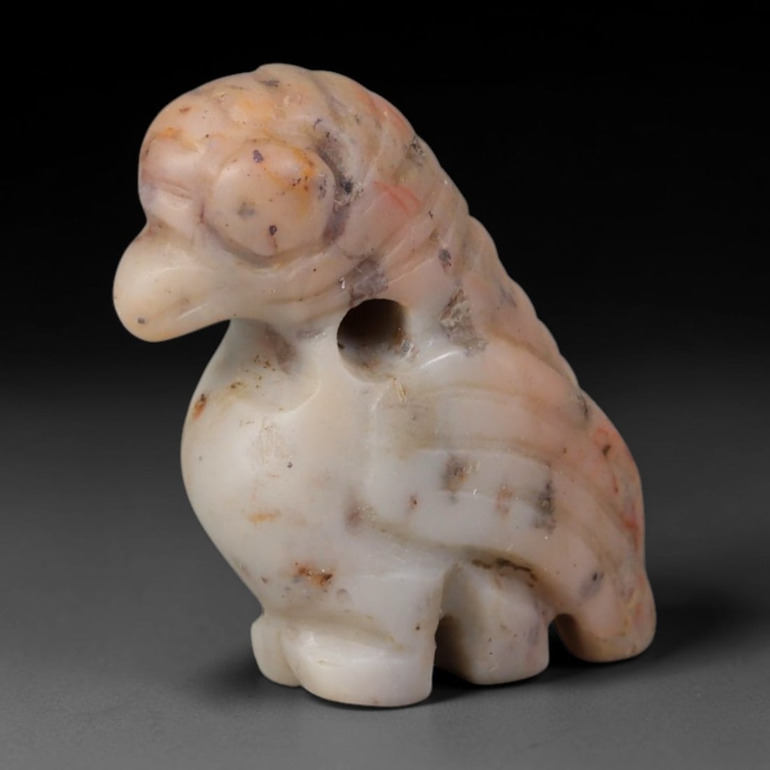 Ancient Western Asiatic Natural Pink Banded Stone Bird Zoomorphic Amulet (1000-600 BCE), 27AB: Hand-carved pale pink marbled stone pendant sculpted as a stylized perched bird figurine. Fine linear incisions detail layered wing plumage, rounded prominent eye and tapered beak; a neat suspension b