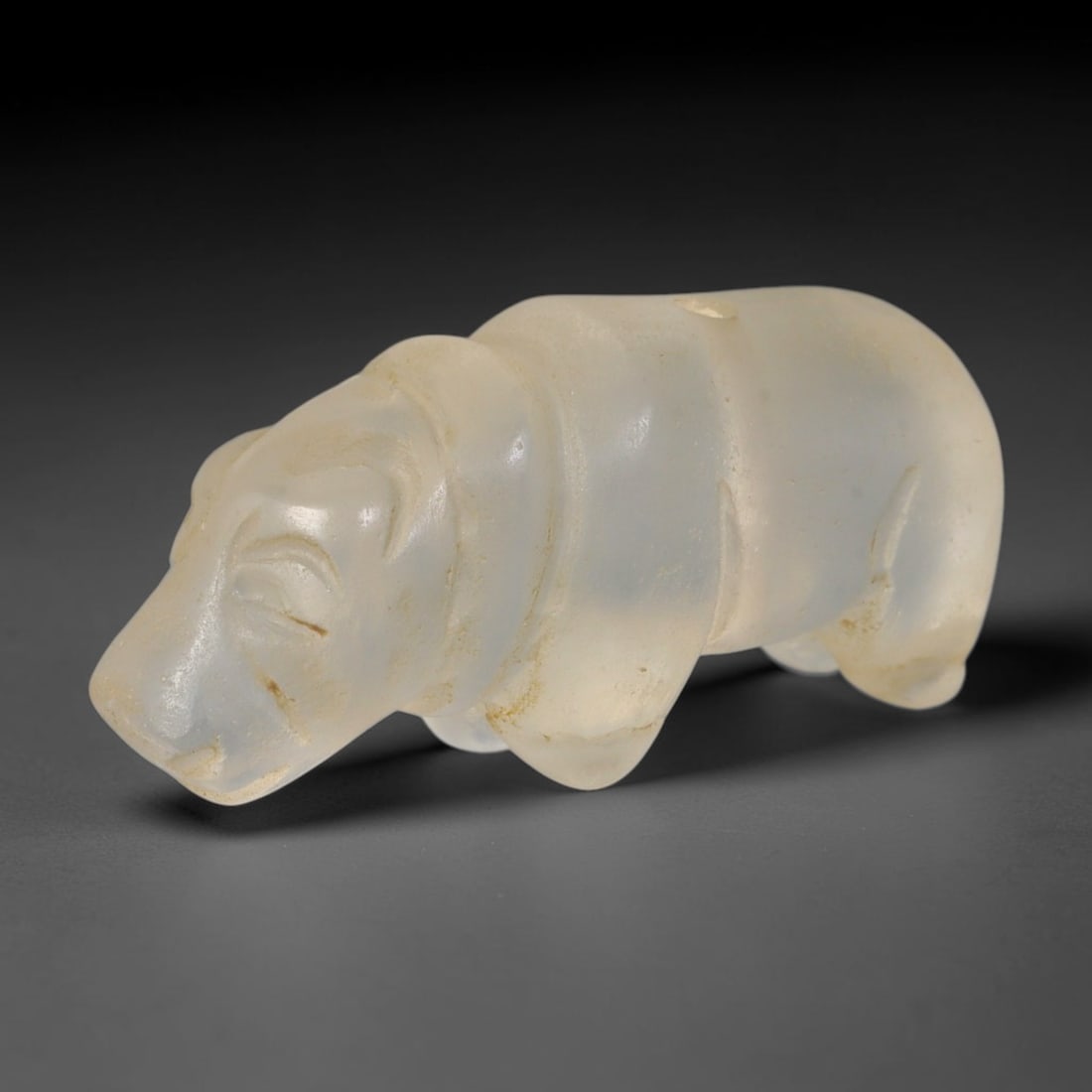 Ancient Southeast Asian Glass Rhinoceros Zoomorphic Amulet (Medieval Period 600-1200 CE), 22AB: Hand-moulded pale translucent glass pendant sculpted into a stylized recumbent rhinoceros form, a sacred protective talisman from ancient Southeast Asian trade and devotional cultures. Subtle incised 