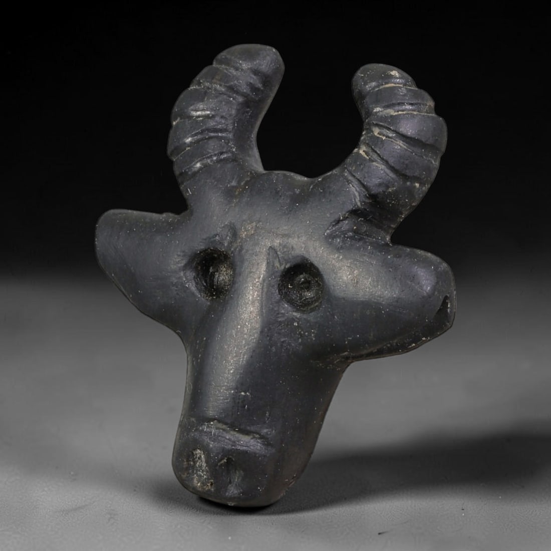 Ancient Levantine Iron Age Black Stone Ram Head Amulet (1200-586 BCE), 95AE: Hand-carved dark polished stone ram head talisman originating from Iron Age Levantine cultures, a sacred symbolic amulet representing fertility, divine favor and sacrificial ritual motifs widely trade