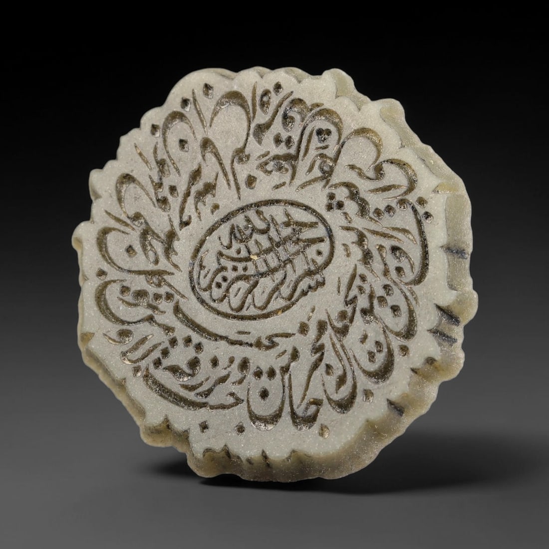 An Islamic Natural Green Stone Circular Script Engraved Talisman Tablet, 28FG: This polished green stone talisman tablet with elaborate concentric layered script engraving covering the central face, framed within a stylized petal-shaped inner border. Fine recessed engraved detai
