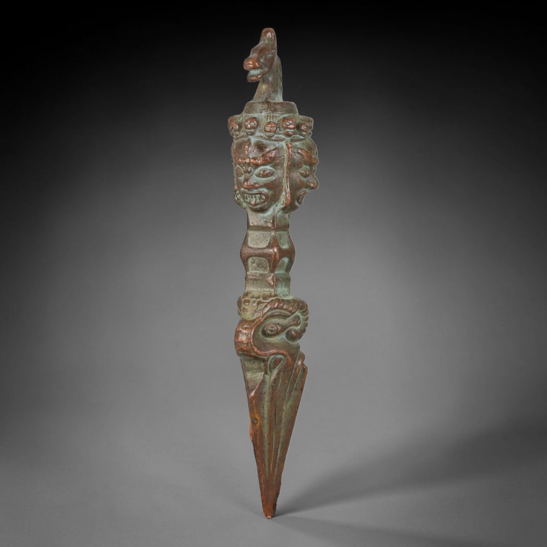 Vintage Tibetan Copper Alloy Multi-Headed Phurba Ritual Dagger, 55AH: Solid cast copper alloy ceremonial phurba dagger featuring intricate relief sculpting throughout its vertical form. The apex is finished with a stylized beast head finial, followed by a tiered section
