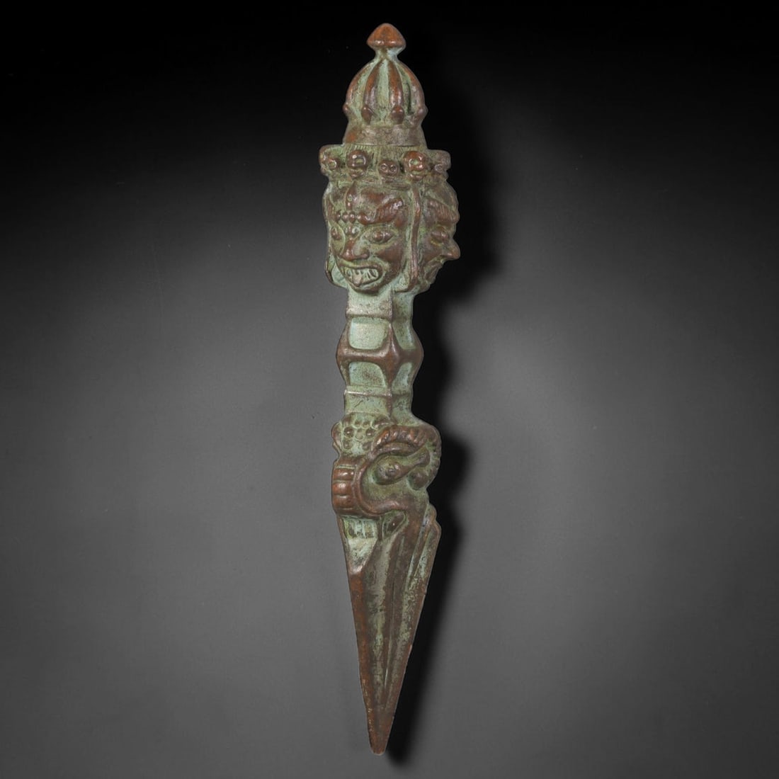 Vintage Tibetan Copper Alloy Multi-Headed Ritual Phurba Dagger, 53AH: Cast copper alloy ceremonial phurba dagger covered in elaborate relief carving along its full vertical length. The top features a tiered crown finial above a section of multi-faced guardian heads rend