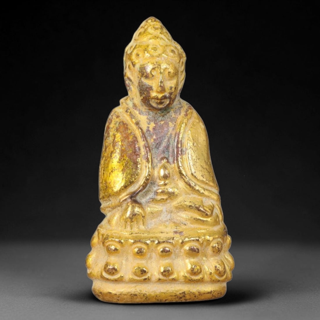 Thai Gilded Metal Mini Sacred Statuette Amulet, 2AH: Compact cast metal sacred figurine covered in gilded finish, featuring carved detailing on the head, robe and embossed pedestal base. Natural discoloration and gentle surface patina are present across