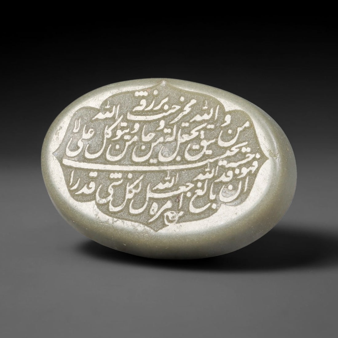 An Islamic Natural Green Stone Circular Script Engraved Talisman Tablet, 30FG: This polished green stone talisman tablet with elaborate concentric layered script engraving covering the central face, framed within a stylized petal-shaped inner border. Fine recessed engraved detai