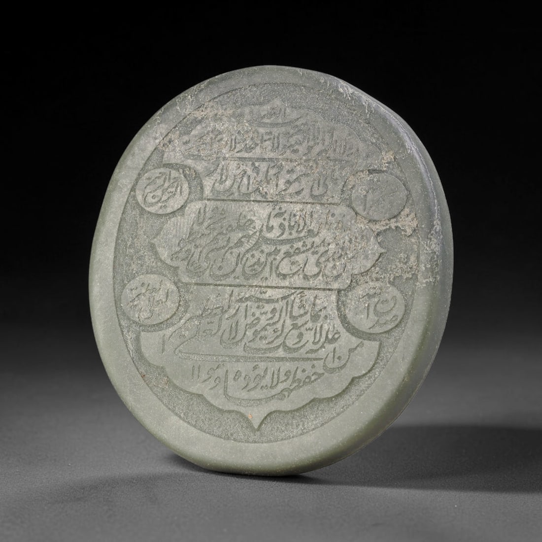 An Islamic Natural Green Stone Circular Script Engraved Talisman Tablet, 45FG: This polished green stone talisman tablet with elaborate concentric layered script engraving covering the central face, framed within a stylized petal-shaped inner border. Fine recessed engraved detai