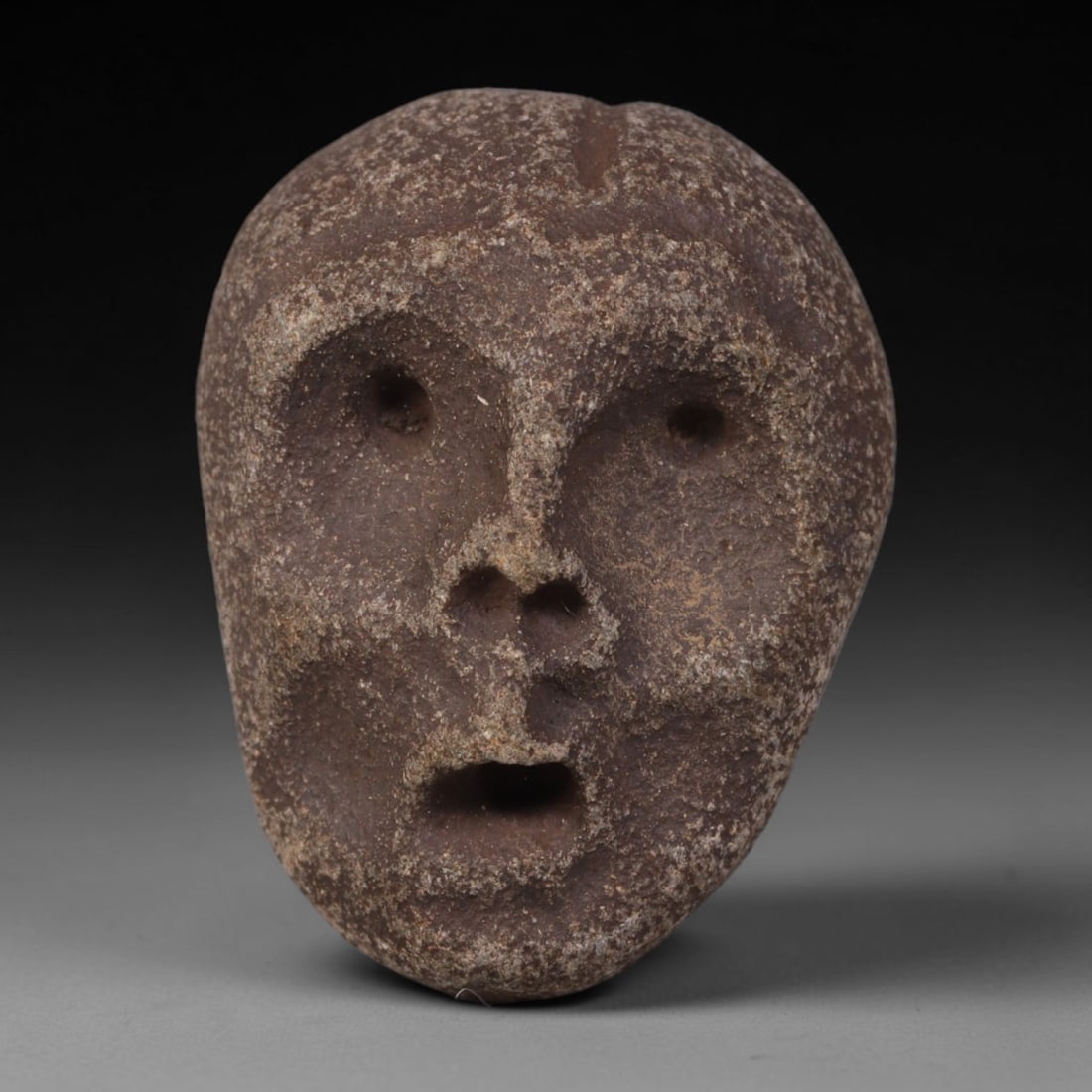 Ancient Medieval Mediterranean Hand Carved Stone Maskette Amulet, 55AP: Miniature wearable sacred talisman hand hewn from natural soft stone, originating from Medieval Mediterranean cultural craft traditions. Small carved stone amulets were widespread personal artifacts a
