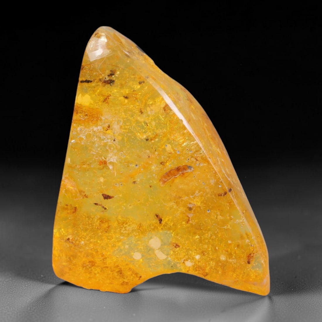22.89ct Natural Baltic Polished Loose Freeform Amber Gemstone, 47AT: This smoothly polished freeform amber piece carries warm translucent organic clarity with fine natural fossil flecks and tiny mineral inclusions suspended throughout its 38x24mm flowing unstructured s