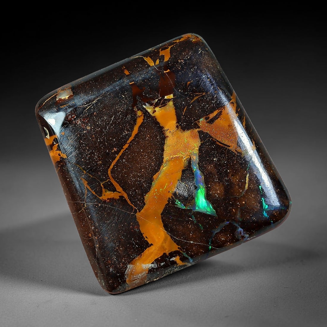 8.47ct Natural Australian Queensland Matrix Boulder Opal Rounded Square Cabochon, 69AV: Hand polished petite rounded square cushion cabochon crafted from natural Queensland matrix boulder opal, featuring deep dark speckled ironstone matrix anchored by a thick sweeping golden-amber opal v