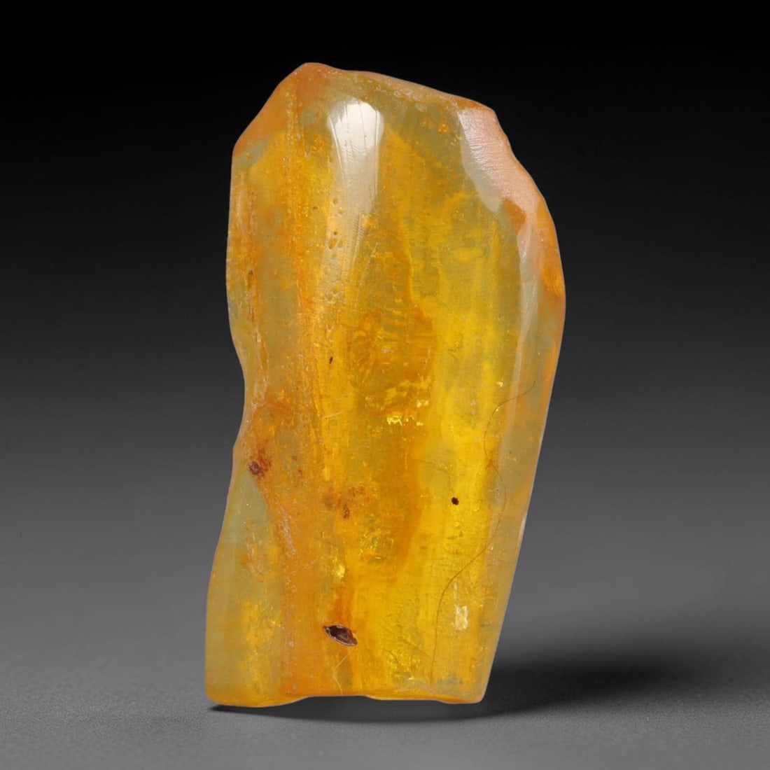 11.57ct Natural Baltic Polished Loose Freeform Amber Gemstone, 19AT: This smoothly polished freeform amber piece carries warm translucent organic clarity with fine natural fossil flecks and tiny mineral inclusions suspended throughout its 32x16mm flowing unstructured s