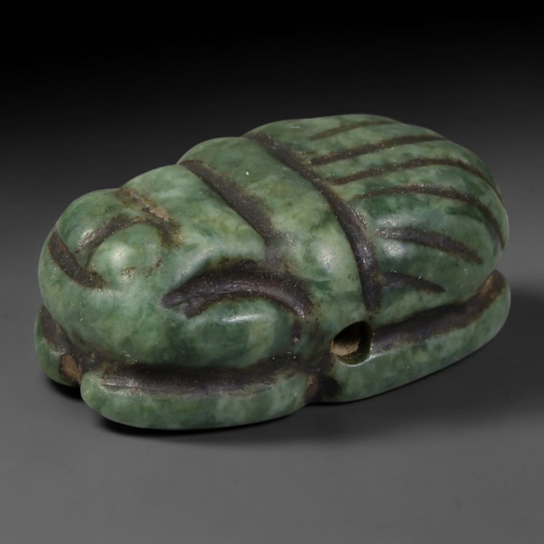 Ancient Egyptian Late Period Natural Green Serpentine Scarab Amulet (664-30 BCE), 59AB: Hand-carved domed scarab pendant crafted from mottled green serpentine stone, featuring crisp incised linear segmentation defining the beetle's head, thorax and wing casings. Dark soil patina fills al