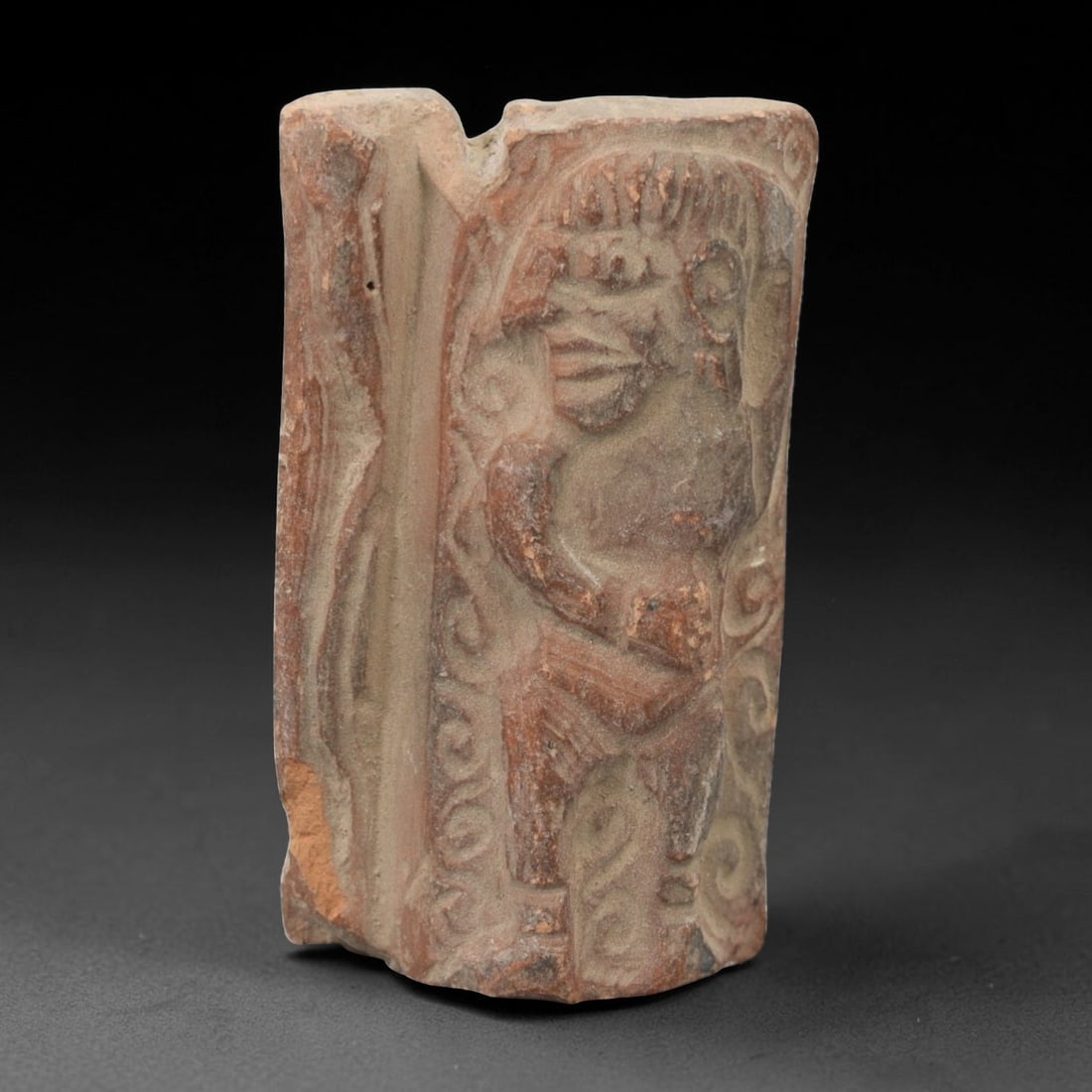 A Near Eastern Terracotta Plaque, 3rd-2nd Millennium BCE, 81FL: Molded from reddish-brown terracotta with natural surface patination and visible edge losses, the object is formed as a rectangular plaque fragment. The relief depicts a standing humanoid figure with 