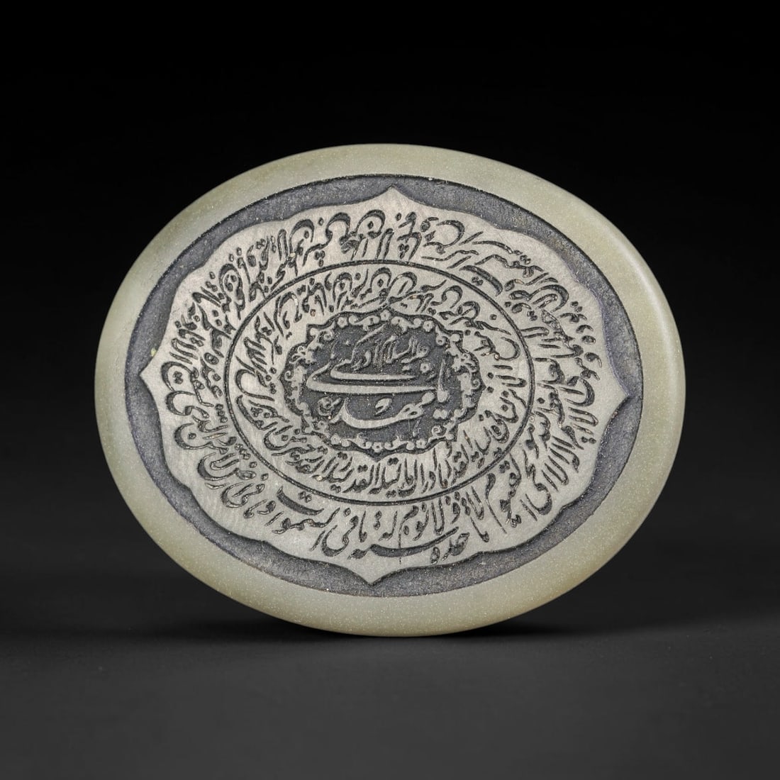 An Islamic Natural Green Stone Circular Script Engraved Talisman Tablet, 36FG: This polished green stone talisman tablet with elaborate concentric layered script engraving covering the central face, framed within a stylized petal-shaped inner border. Fine recessed engraved detai