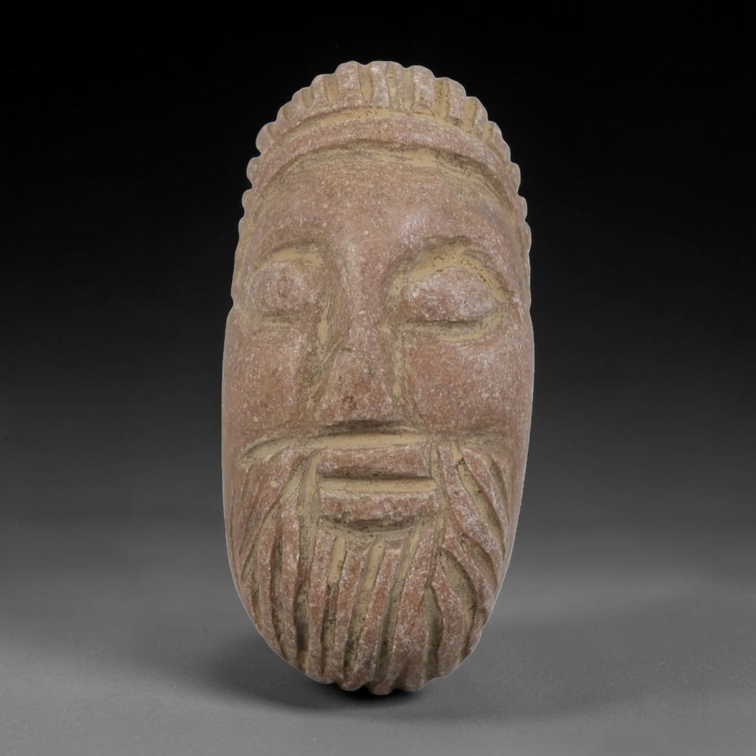 Antique Islamic Carved Stone Bearded Bust Intaglio, 86AN: Carved from soft, weathered pinkish stone, this elongated intaglio depicts a stylized bearded male face in relief. The figure features closed eyes, a straight nose, and a neatly carved beard with vert