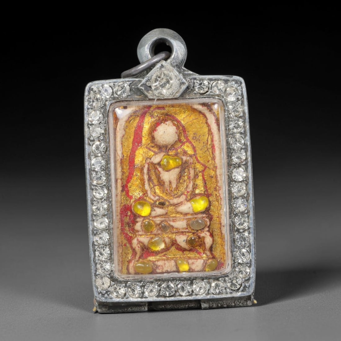 Thai Buddhist Folk Tradition Enclosed Amulet Pendant with Decorative Metal Casing, 24AH: This Thai sacred amulet is housed within an ornate hinged metal protective casing fitted with a top loop for wear as a pendant. The casing features intricate embossed surface detailing and a continuou
