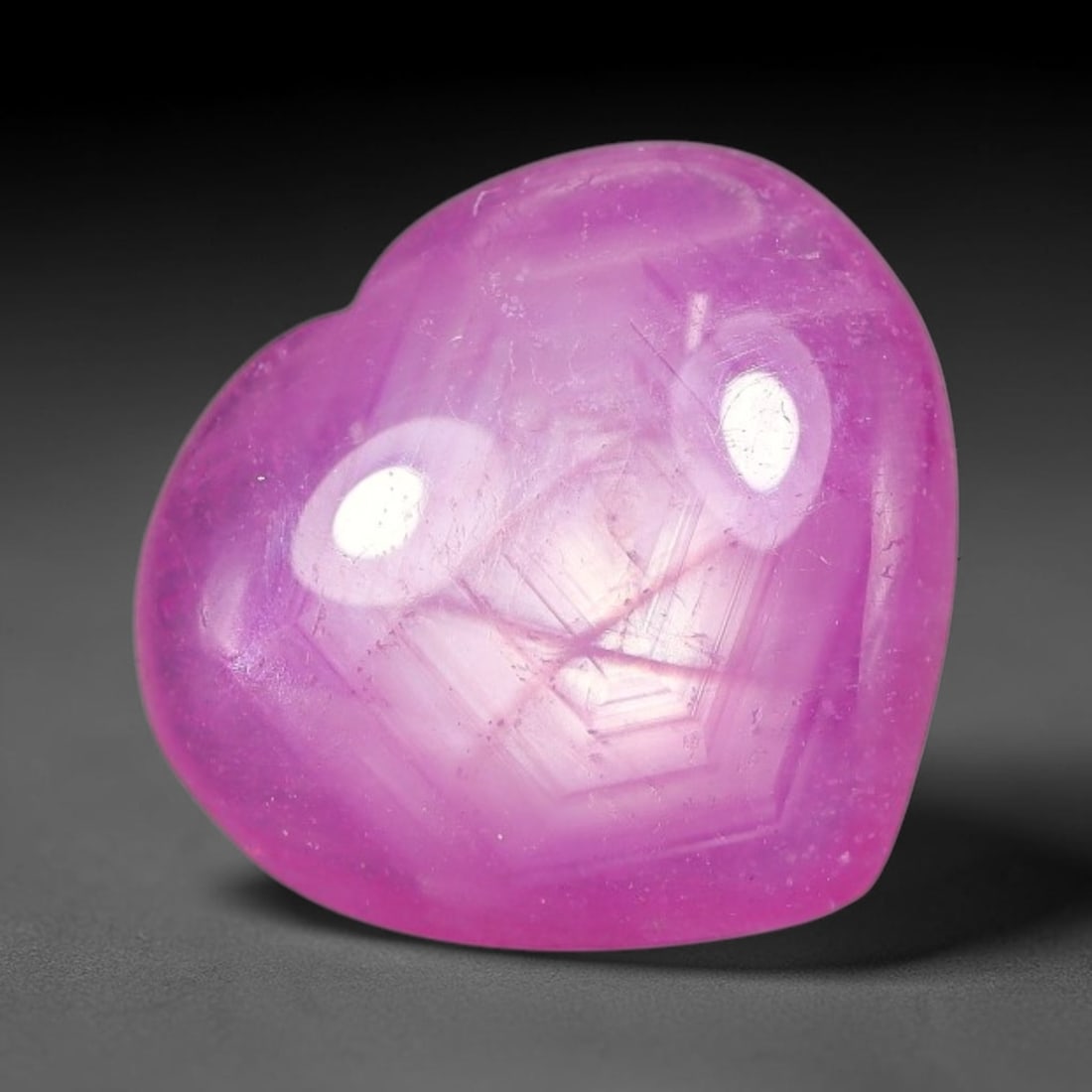 7.74 Carats Natural Mozambique Hot Pink Ruby Loose Gemstone, 63FE: This heart shaped Mozambique ruby cabochon measures 12.8x11.8x4.7mm, showcasing a vivid saturated hot pink body paired with stunning natural hexagonal crystal growth banding that forms a distinct geom