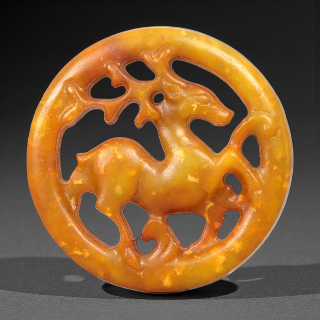A Chinese Hetian Jade Openwork Deer Plaque, 52FH: Carved from warm honey-yellow Hetian jade with mottled tonal variation and natural inclusions, the plaque is circular in form and executed in openwork. The central motif depicts a standing deer shown 