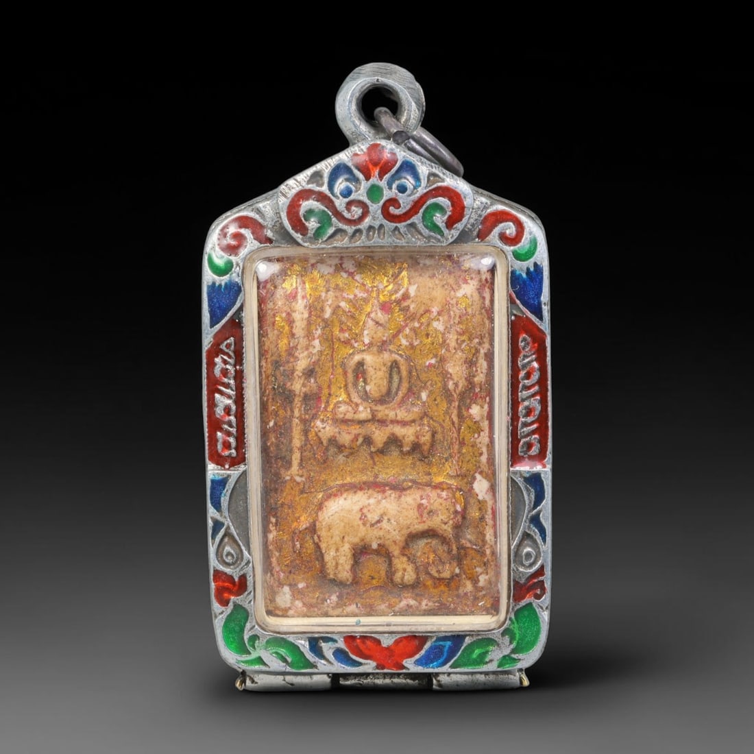 Thai Buddhist Folk Tradition Enclosed Amulet Pendant with Decorative Metal Casing, 18AH: This Thai sacred amulet is housed within an ornate hinged metal protective casing fitted with a top loop for wear as a pendant. The casing features intricate embossed surface detailing and a continuou