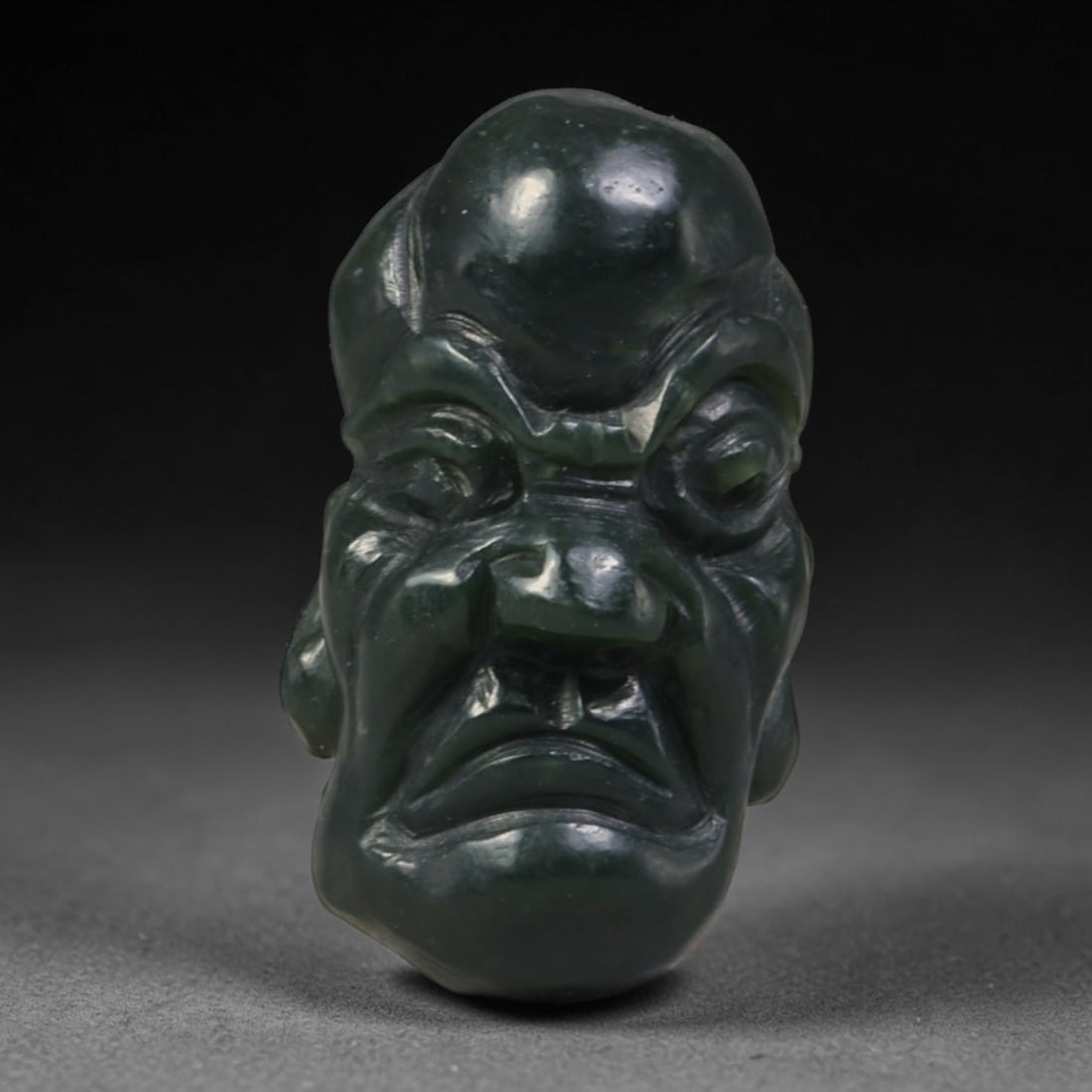 Natural Vintage Chinese Nephrite Jade Deep Dark Green Arhat Head Carved Face Bead, 96AA: Hand-carved vintage Chinese strung bead crafted from natural vintage Chinese nephrite jade, measuring 3cm x 1.8cm. This barrel-shaped bead is intricately sculpted as a distinctive asymmetrical Buddhis