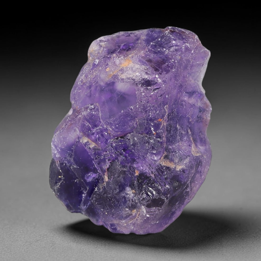 186ct Natural Chinese Deep Violet Purple Fluorite Rough, 5AT, 5AT: This rugged fluorite rough boasts rich layered violet purple saturation blended with warm rust-colored mineral inclusions that streak its uneven raw surface, soft translucency lets light drift through